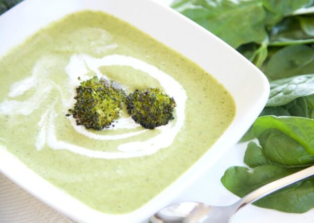 Rectangular white bowl with vibrant green broccoli soup and fresh spinach.