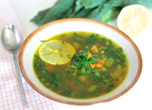 Turmeric and kale soup with ground lamb in a bowl with spoon and half a lemon.