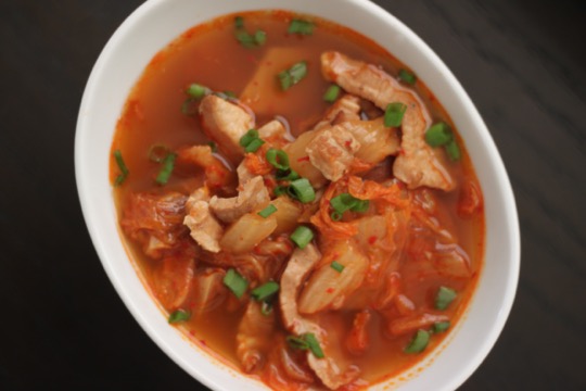 Overhead shot of large oval bowl of pork belly soup in red broth.