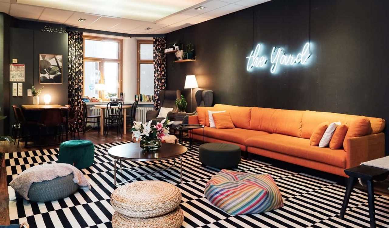 Chic common room at the Yard Hostel in Helsinki, Finland, with an orange couch, puffs for sitting on, and a neon sign saying 