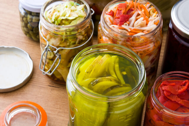 Overhead shot of colorful fermented preserved vegetables in jars on a wooden table.