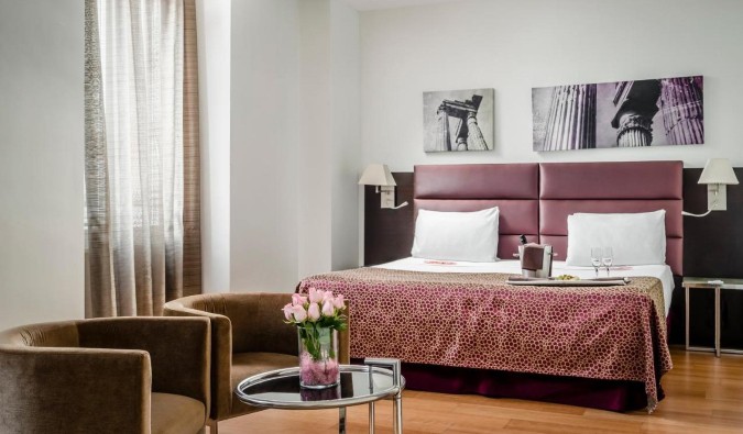 A guestroom with pink accents throughout, including roses in a vase on a low table at Eurostars Roma Aeterna hotel in Rome, Italy