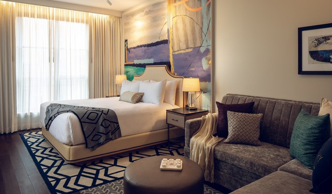 Deluxe king guestroom at the Sophy Hyde Park hotel in Chicago, decorated in a contemporary style with a king sized bed and a grey sectional couch