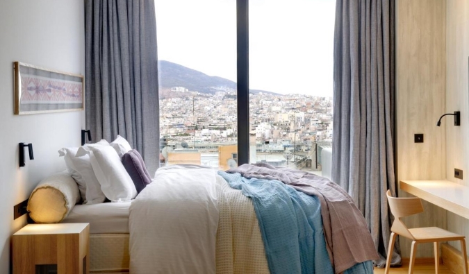 Simple but cozy guestroom at Coco-Mat Hotel with floor to ceiling windows looking out over the city of Athens, Greece