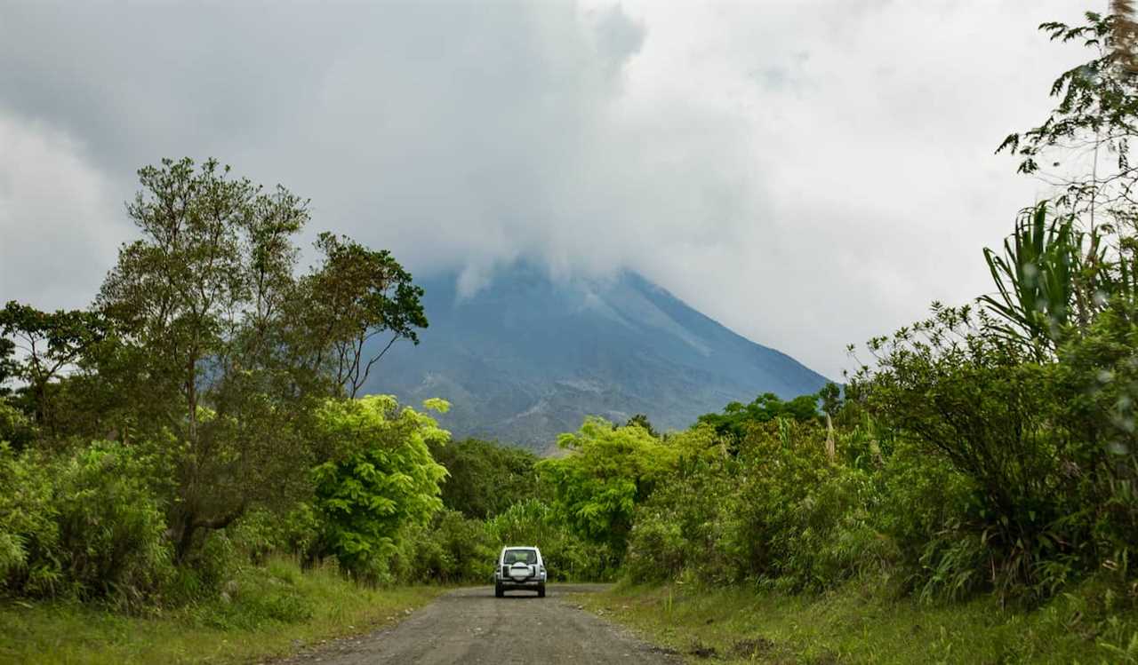 A car driving on a dirt road in the shadow of Arenal volcano in Costa Rica