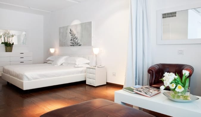 A king-sized bed, coffee table, leather armchair, and vases of flowers around in a suite at Magna Pars L'Hotel a Parfum, a five-star hotel in Milan, Italy