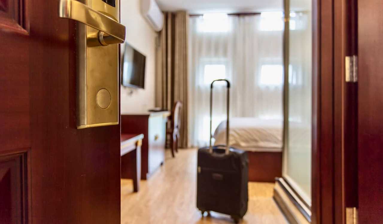 A small rolling suitcase standing near the door in a cozy hotel room abroad