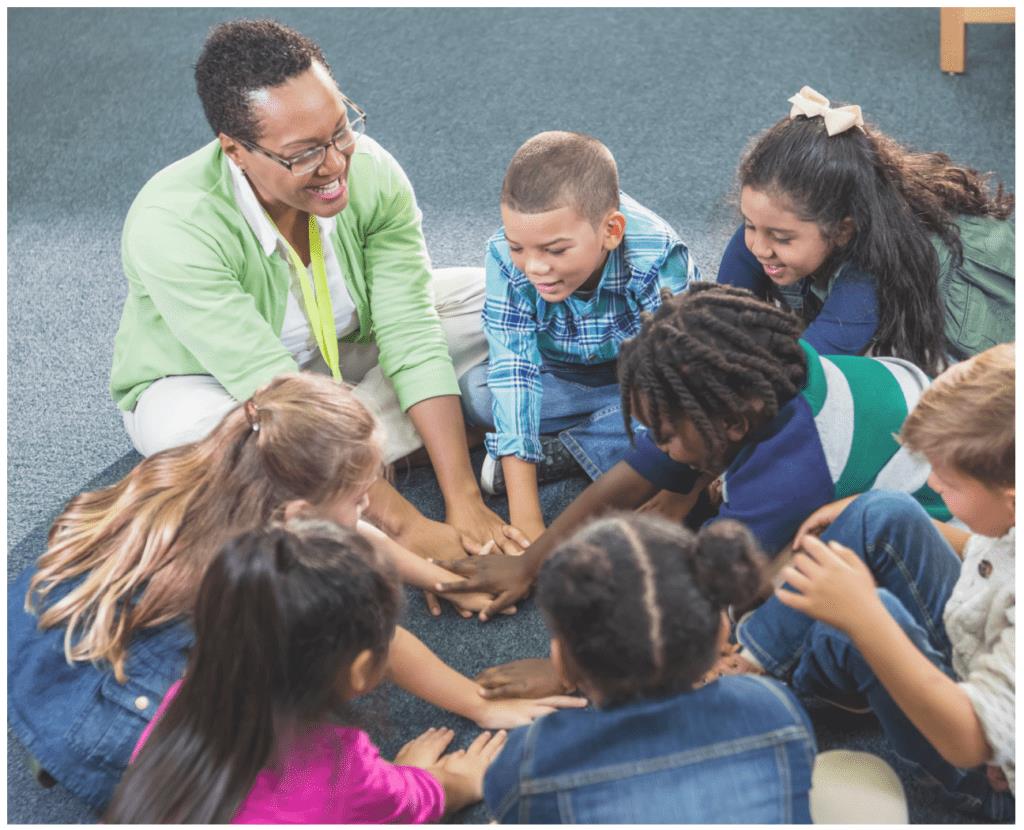 Teacher and students sitting on the floor together stacking hands