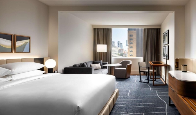 A large guestroom with a king-sized bed, couch, seating area, large windows, all decorated in a minimal contemporary design at the Park Hyatt hotel in Toronto, Canada