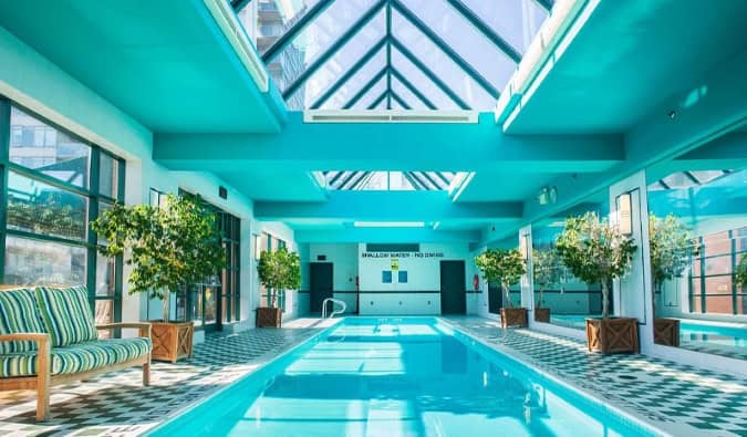 A long indoor swimming pool lined with small potted trees in a glass atrium at the Yorkville Royal Sonesta hotel in Toronto, Canada