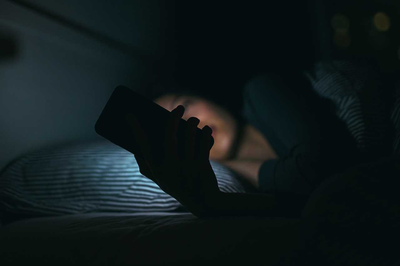 Young woman texting while lying in bed at night