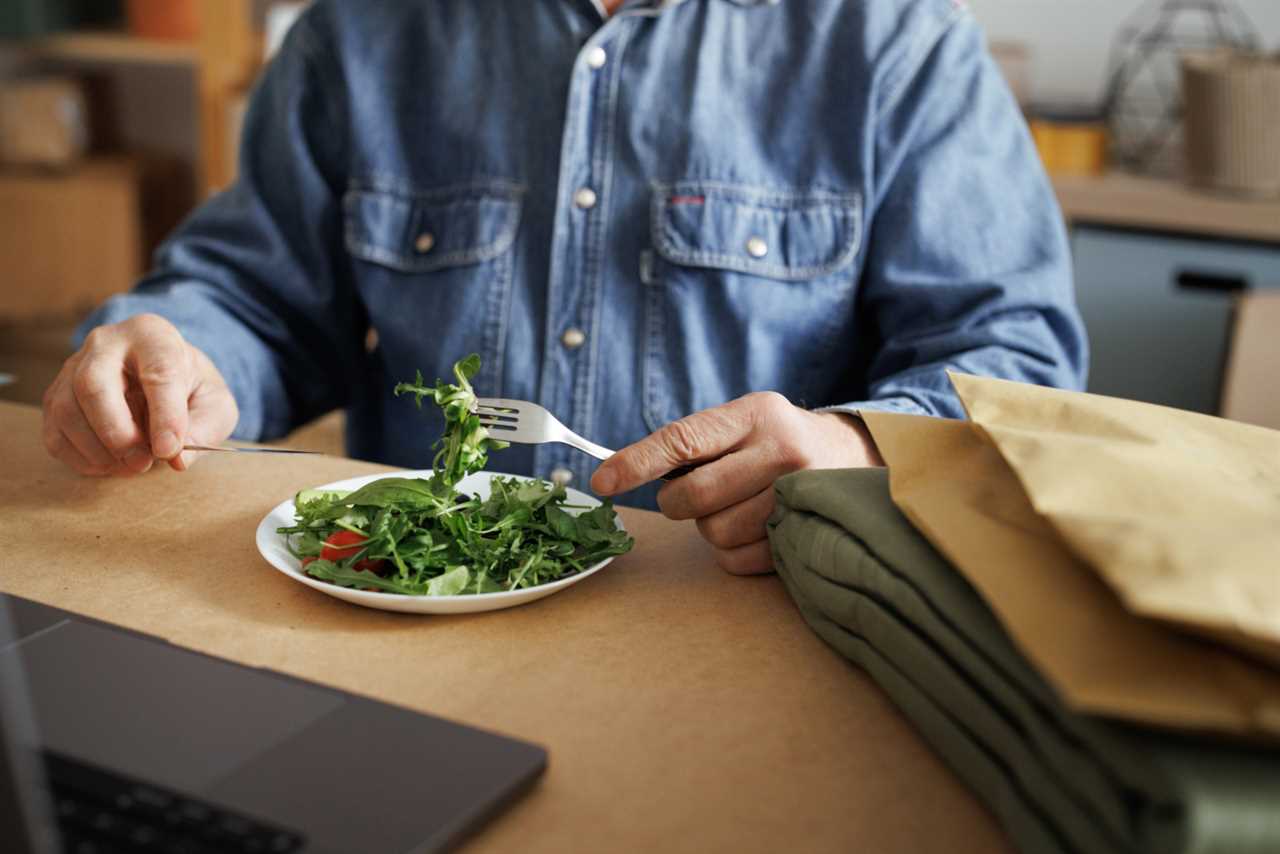 Unrecognizable senior man eating salad while working at home