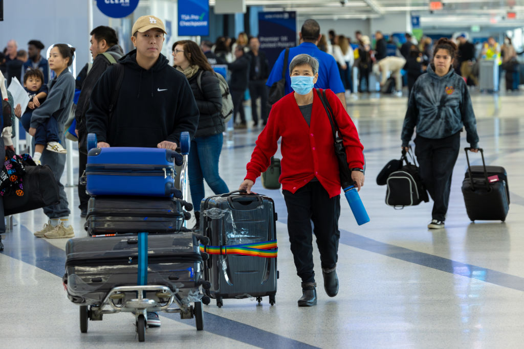 Travelers at LAX airport, including a woman wearing a mask.