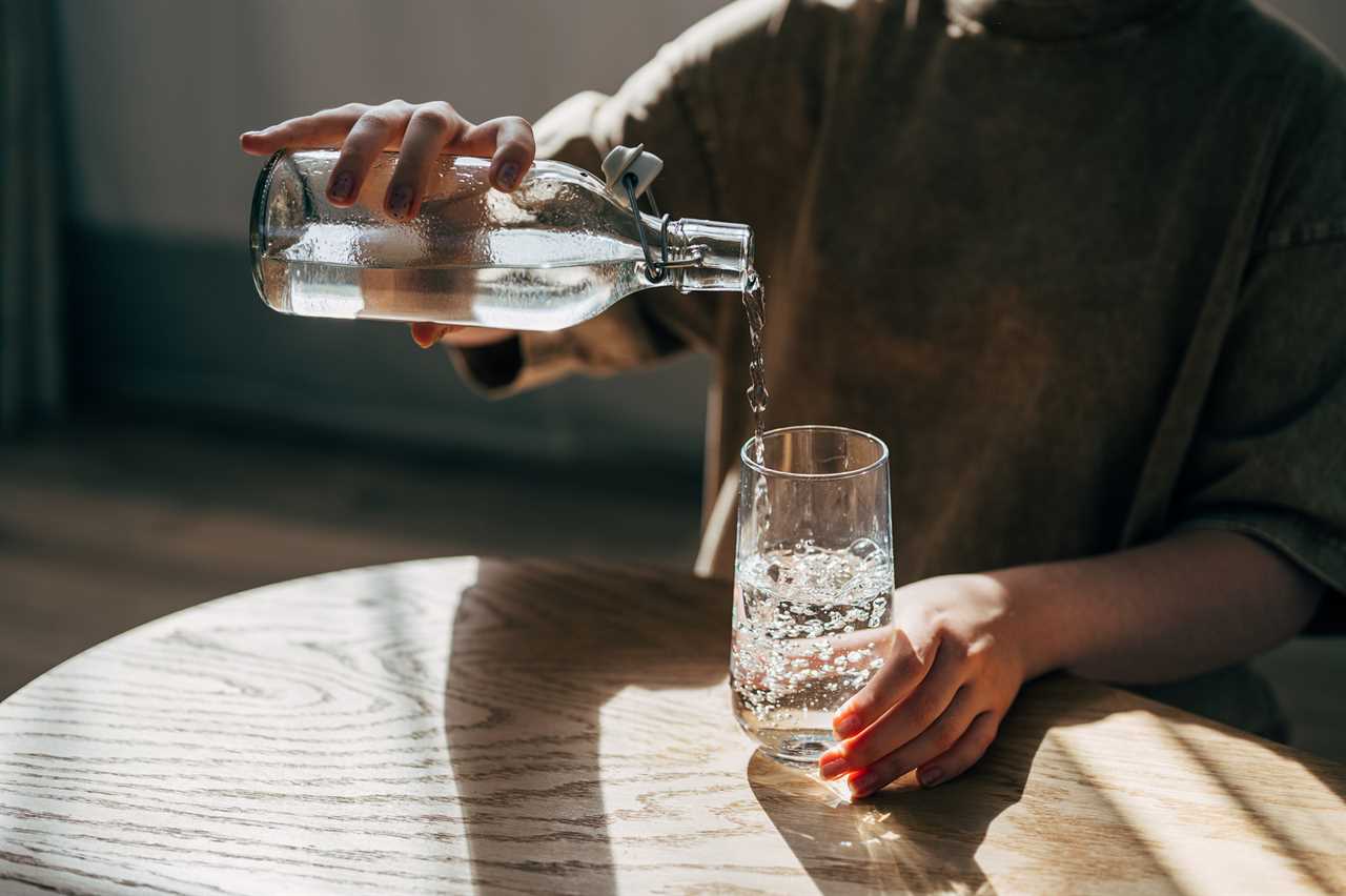 a woman at the table pours a glass of water from a bottle