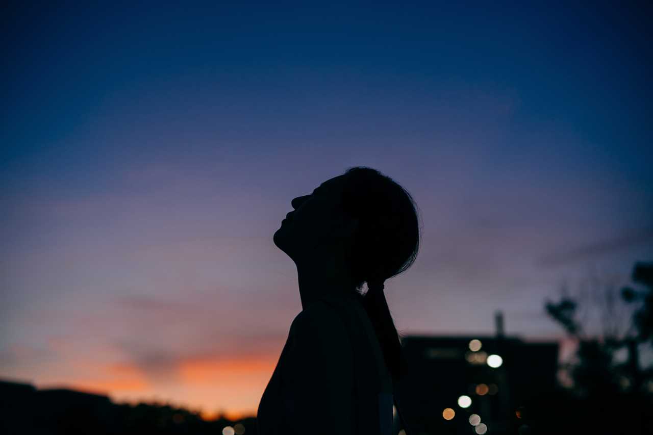 Silhouette of the side profile of young Asian woman looking over sky enjoying twilight in the nature. Freedom in nature. Connection with nature