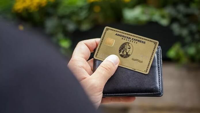 The American Express® Gold Card being held up in front of a bright blue wall