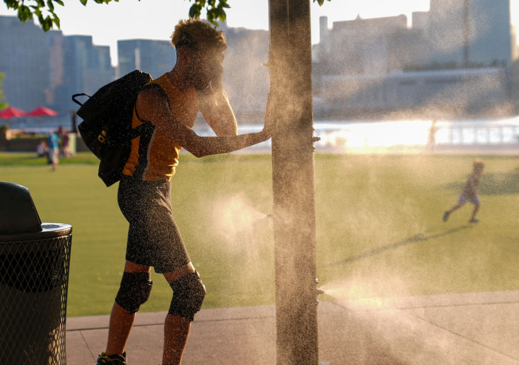 A man tries to cool off with a sprinkler that helps people cool off in New York City on July 15, 2024.